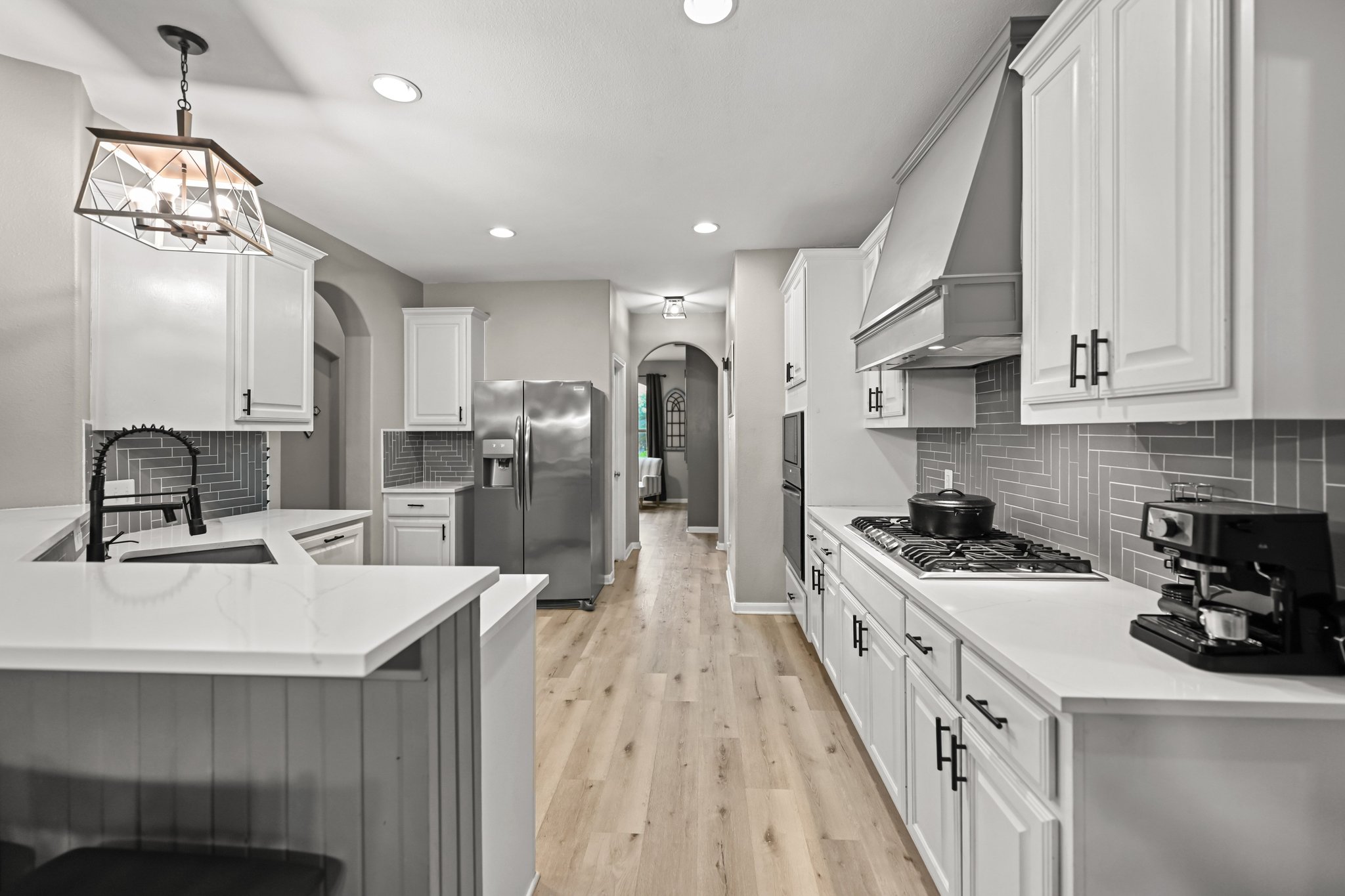 5528 Wild Foxglove Road Spicewood, TX 78669 - Photo 6 of 38 Elongated kitchen featuring white cabinetry, light countertops, wood-finish flooring, a herringbone tile backsplash, and stainless steel appliances
