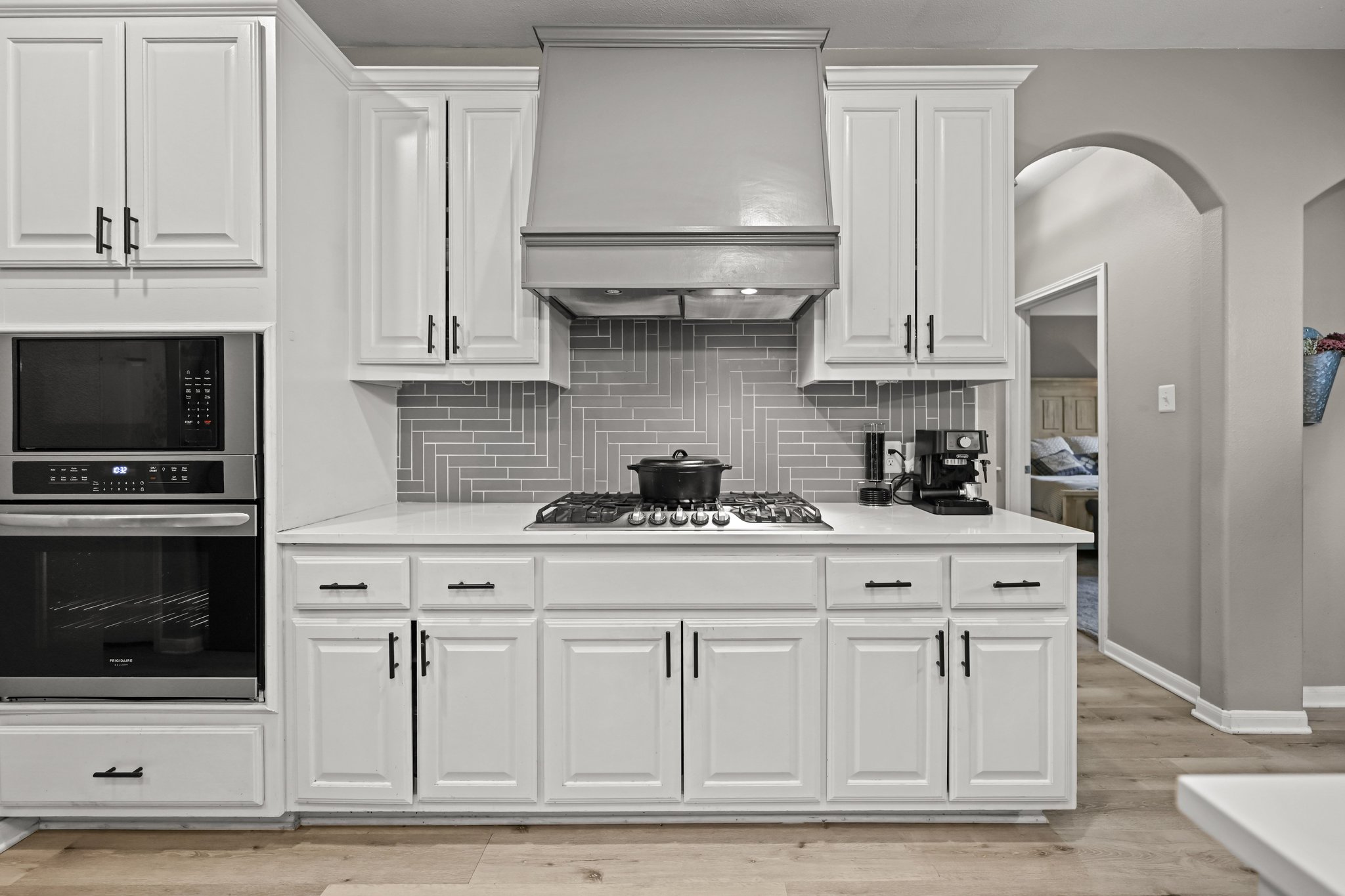 5528 Wild Foxglove Road Spicewood, TX 78669 - Photo 8 of 38 Kitchen featuring white shaker-style cabinetry, a gray subway tile backsplash in a herringbone pattern, a gas range with a stainless steel vent hood, and a built-in stainless steel microwave and oven combination