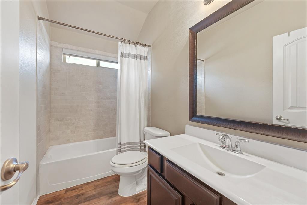 409 Harding Lane Lavon, TX 75166 - Photo 7 of 34 Bathroom featuring a bathtub with subway tile surround, wood-finish flooring, a dark wood vanity with an integrated sink, and a framed mirror