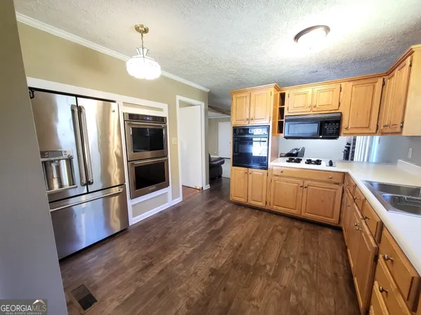 a kitchen with stainless steel appliances kitchen island granite countertop a refrigerator a oven a stove and a wooden floors