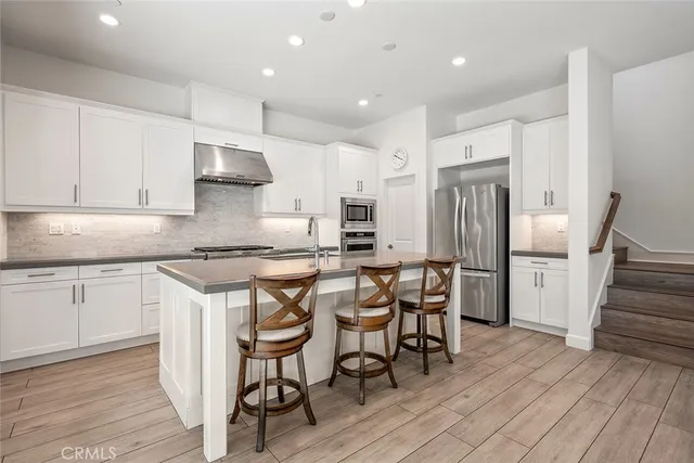 a kitchen with stainless steel appliances granite countertop a stove top oven a sink dishwasher a dining table and chairs with wooden floor