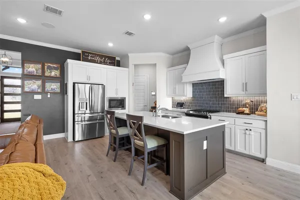 a kitchen with stainless steel appliances a stove a sink a refrigerator white cabinets and couches with wooden floor