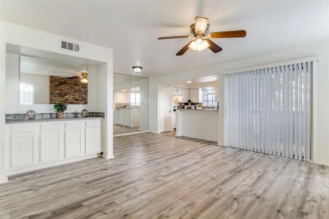 a view of an empty room and kitchen view with wooden floor