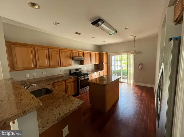 a kitchen with stainless steel appliances granite countertop a refrigerator a sink dishwasher a stove and white countertops with wooden floor