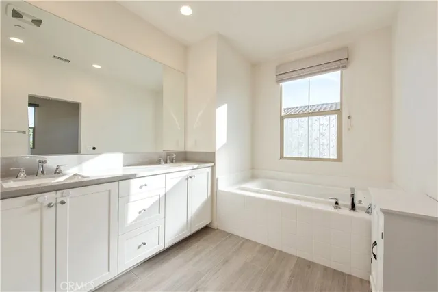 a bathroom with a double vanity sink a large mirror and a bathtub