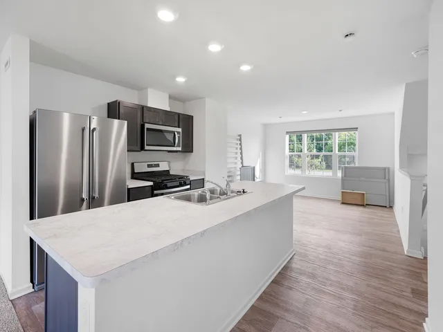 a large kitchen with stainless steel appliances a large counter top a refrigerator a stove a sink dishwasher a oven with white cabinets and wooden floor