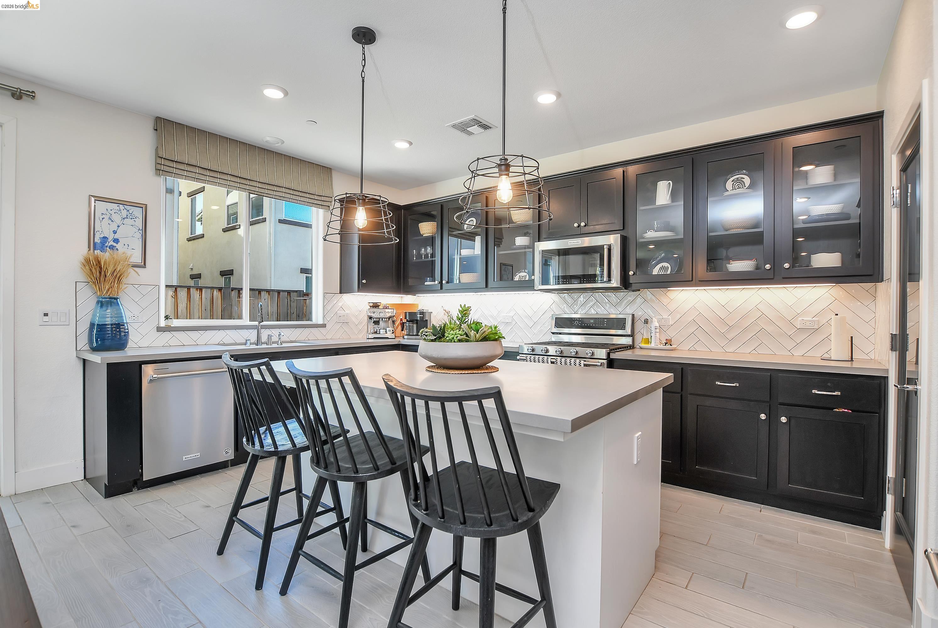 829 Hardcastle Ranch Road Oakley, CA 94561 - Photo 13 of 41 Kitchen featuring black cabinetry, stainless steel appliances, a white herringbone tile backsplash, an island with a light countertop, and wood-finish flooring