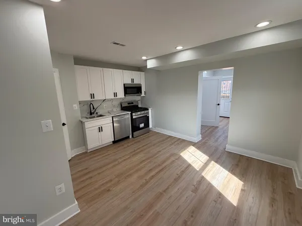 a kitchen with stainless steel appliances a sink a stove a refrigerator cabinets and a wooden floor