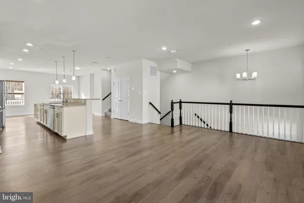 a view of an empty room with wooden floor and a kitchen