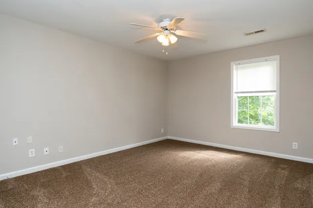 an empty room with a chandelier fan and windows
