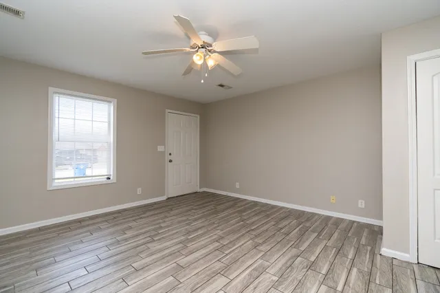 an empty room with wooden floor fan and windows