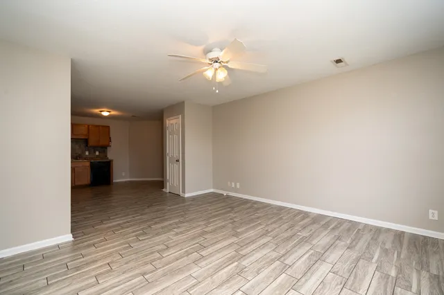a view of an empty room with wooden floor and a ceiling fan