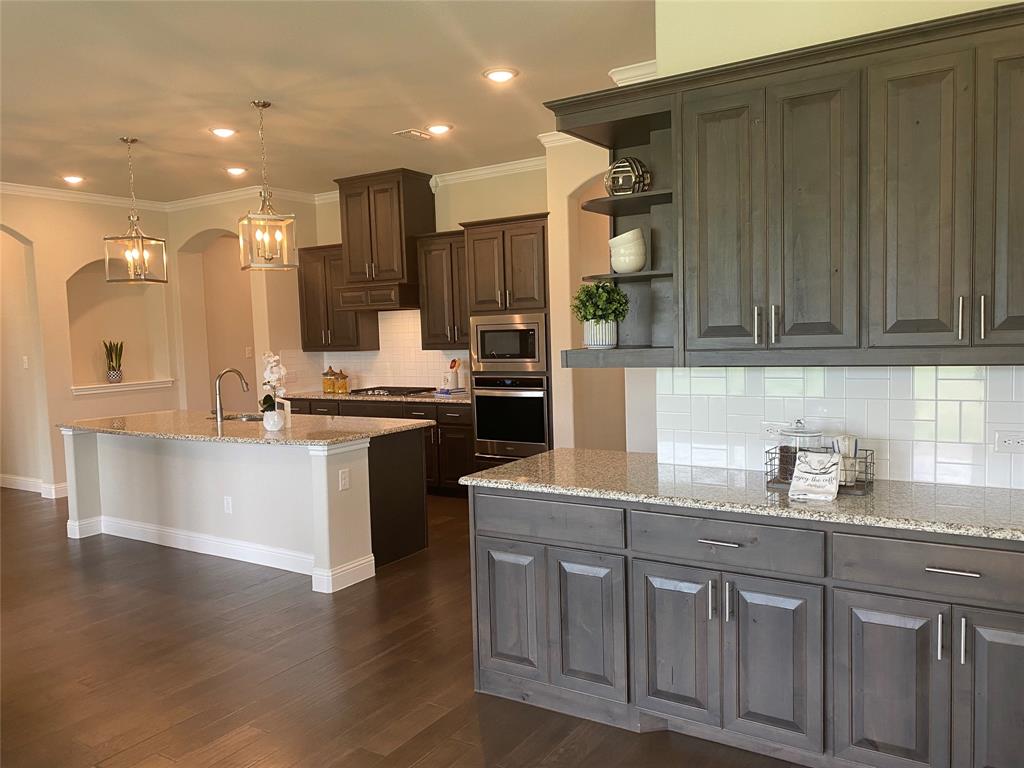 209 Johnson Street Granbury, TX 76048 - Photo 13 of 40 Kitchen featuring decorative light fixtures, dark hardwood / wood-style flooring, backsplash, appliances with stainless steel finishes, and a center island with sink