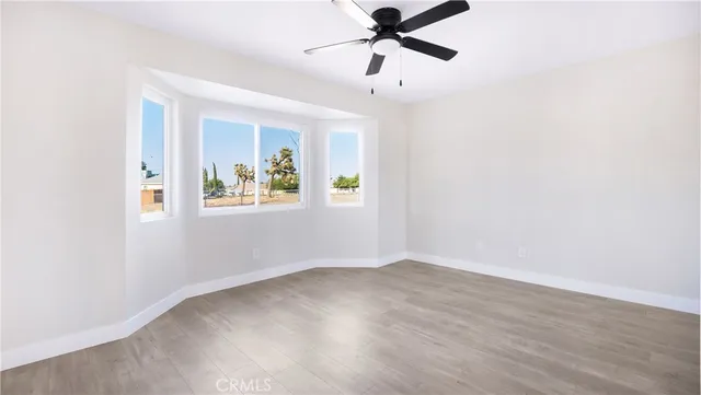 an empty room with wooden floor ceiling fan and windows