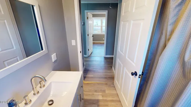 a view of a hallway with wooden floor and a bathroom
