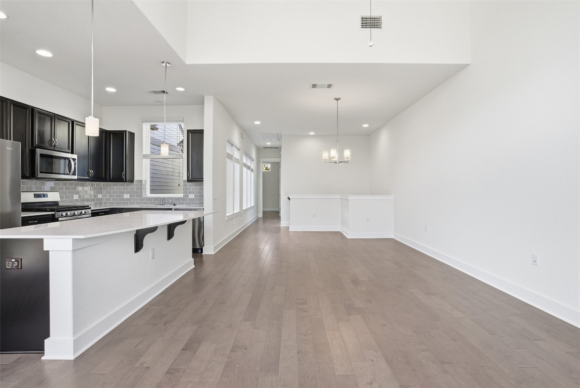12604 Red Sparrow Street, Unit 14 Austin, TX 78729 - Photo 20 of 40 Kitchen featuring dark cabinetry, backsplash, a breakfast bar area, appliances with stainless steel finishes, and hanging light fixtures