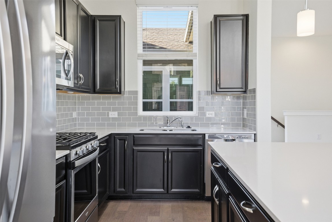12604 Red Sparrow Street, Unit 14 Austin, TX 78729 - Photo 24 of 40 Kitchen featuring stainless steel appliances, dark cabinets, decorative backsplash, dark wood-style flooring, and hanging light fixtures