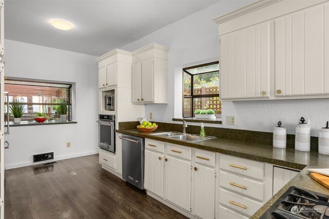 a kitchen with granite countertop white cabinets a sink a window and stainless steel appliances