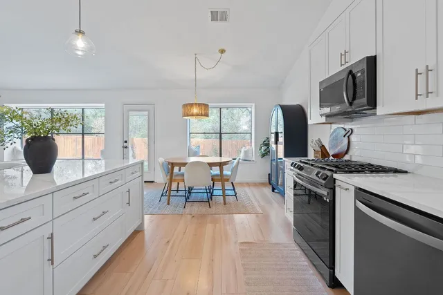 a kitchen with stainless steel appliances granite countertop a stove a refrigerator a kitchen island a dining table and chairs with wooden floor