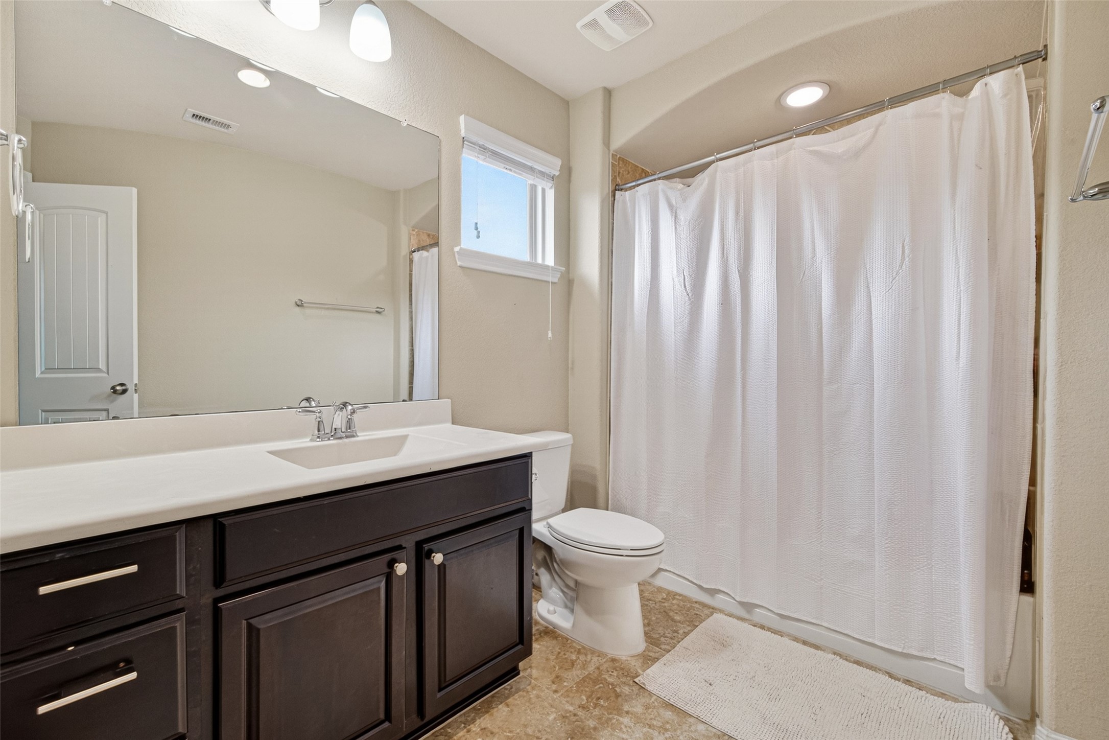 25611 Ellis Ridge Court Katy, TX 77494 - Photo 29 of 49 This bathroom features a modern design with a dark wood vanity, a large mirror, and overhead lighting. It includes a shower-tub combo with a white curtain, beige tile flooring, and a small window for natural light.