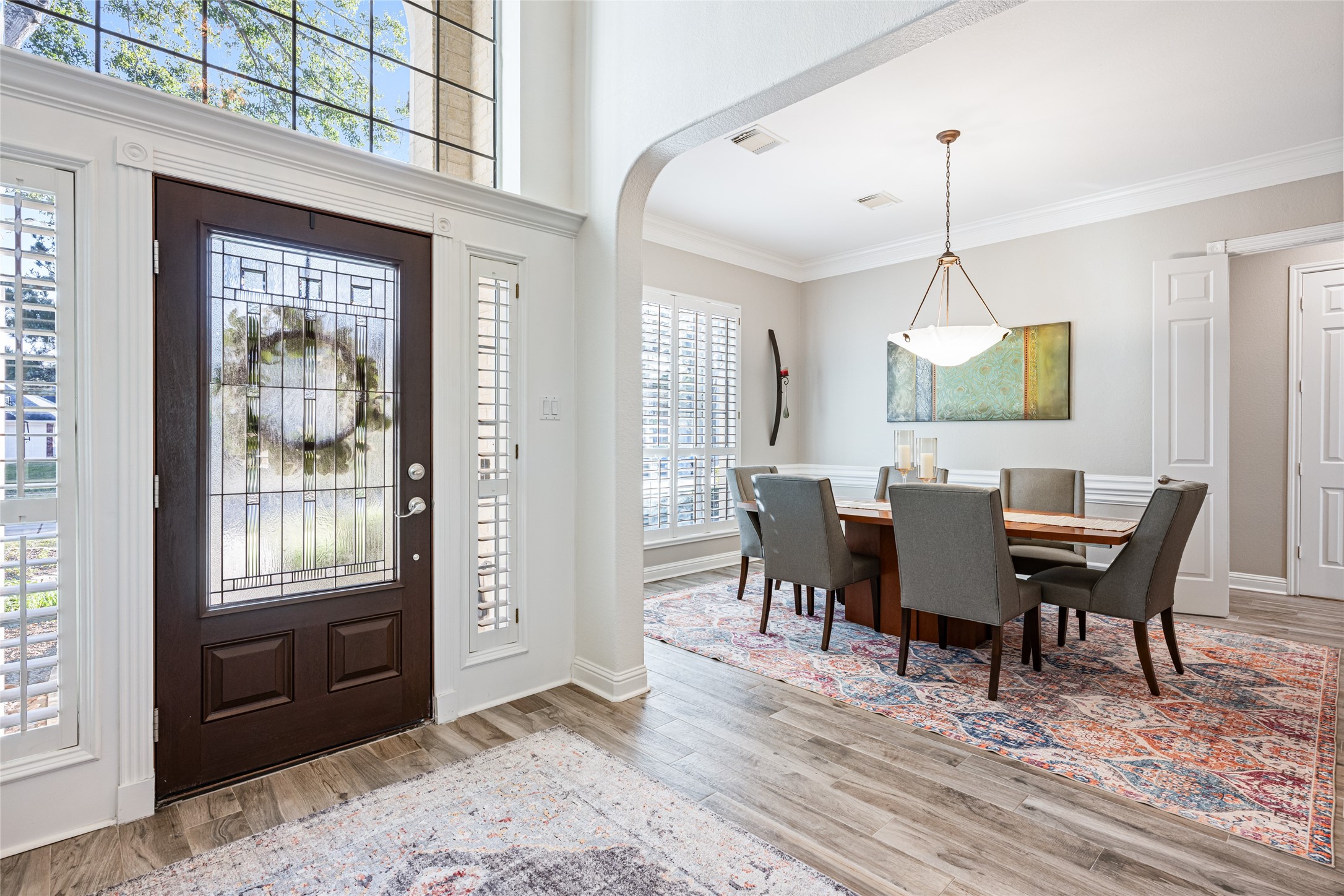 22806 2 Rivers Lane Katy, TX 77450 - Photo 13 of 49 Elegant entryway features wood-look tile flooring, a decorative glass front door, and abundant natural light. The adjacent formal dining room showcases crown molding, modern designer lighting, and custom plantation shutters, creating a refined yet welcoming space for entertaining.