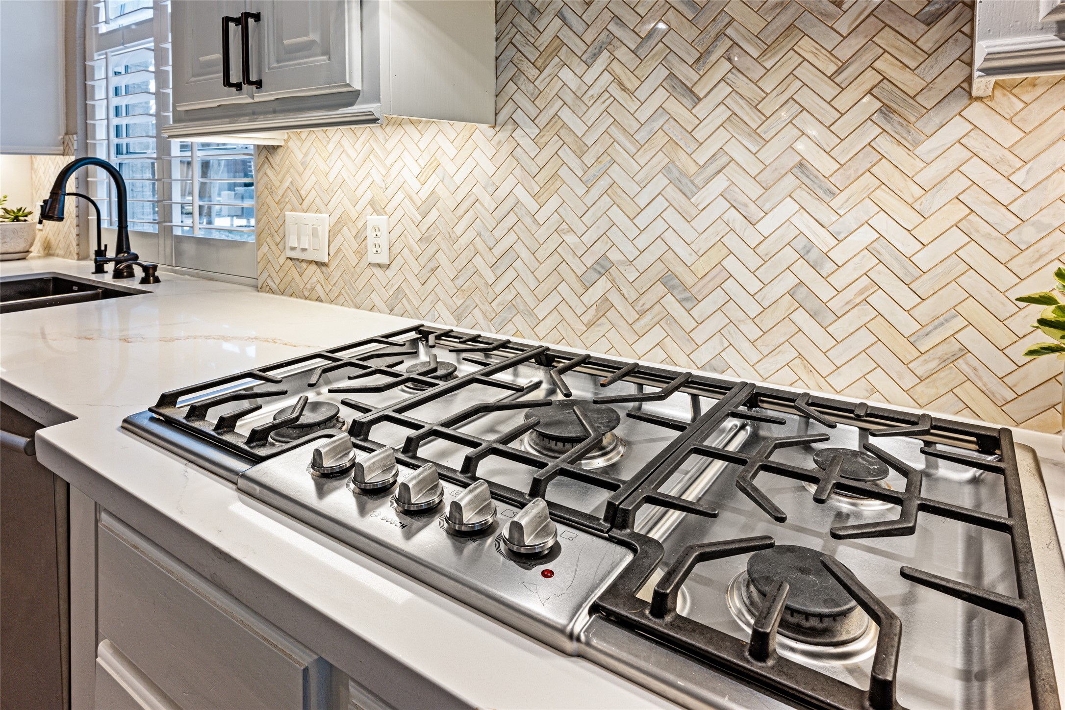 22806 2 Rivers Lane Katy, TX 77450 - Photo 22 of 49 This kitchen features a sleek gas stovetop set in a bright, modern countertop. The backsplash is a stylish herringbone pattern, complementing the clean lines of the cabinetry. A nearby sink with a contemporary faucet and ample natural light enhance the space's functionality and appeal.