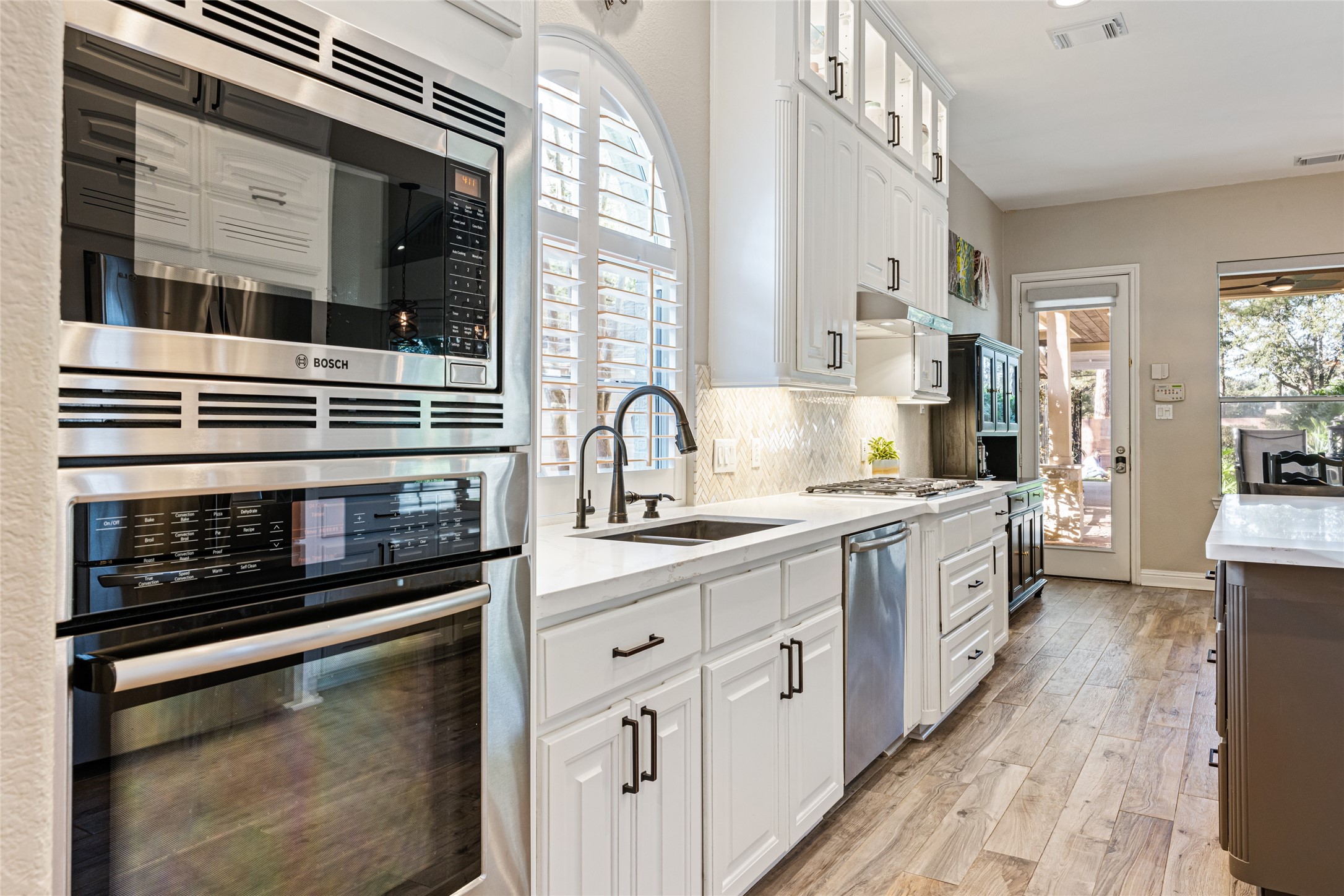 22806 2 Rivers Lane Katy, TX 77450 - Photo 23 of 49 This kitchen features modern stainless steel appliances, white cabinetry with rubbed bronze hardware, and a sleek, light-filled design. The wood-look flooring adds warmth, while the large window and glass door provide ample natural light and access to your outdoor oasis.