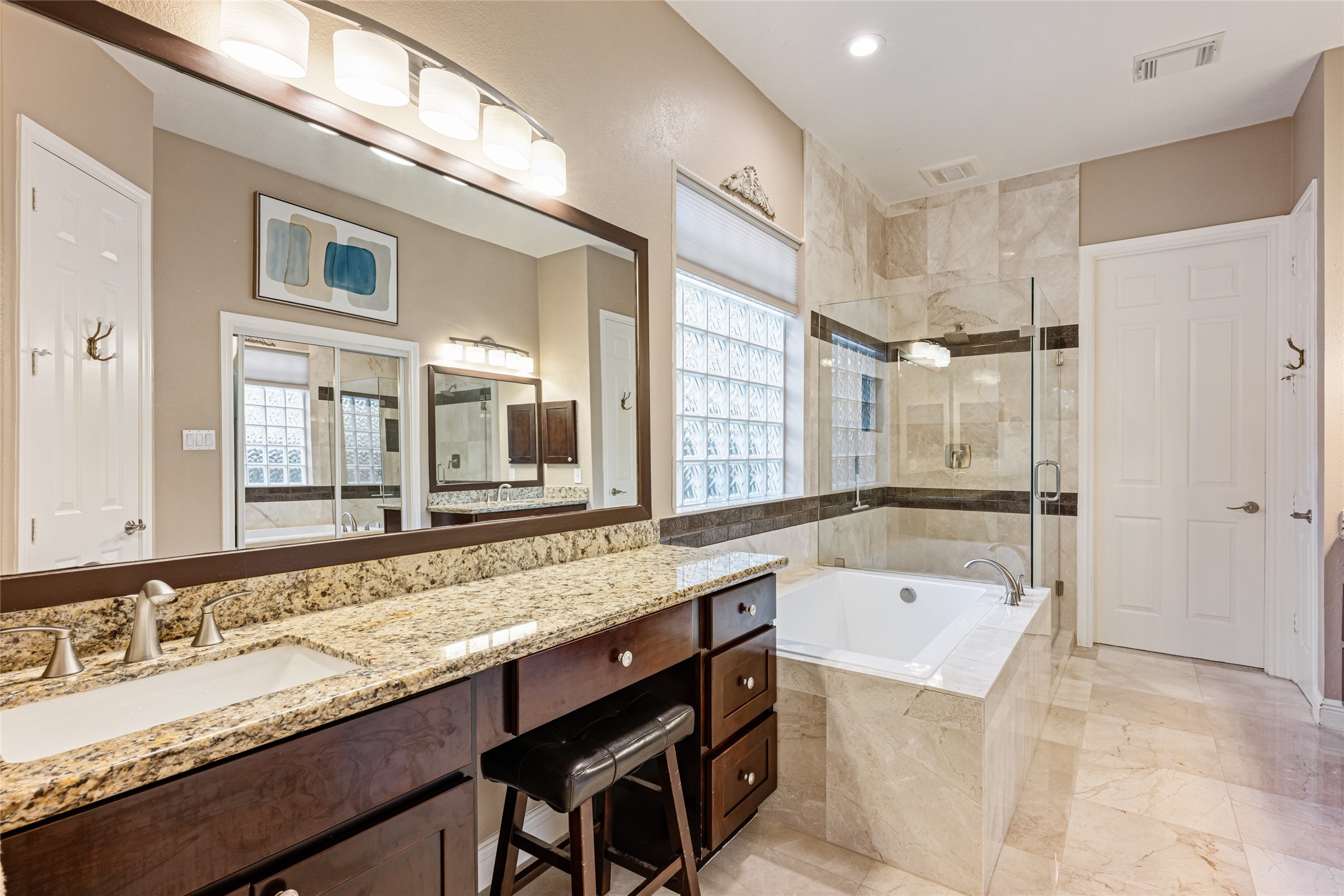 22806 2 Rivers Lane Katy, TX 77450 - Photo 29 of 49 This elegant bathroom features a spacious granite countertop with dual sinks, a large mirror, and a stylish vanity. It also includes a luxurious soaking tub and a separate glass-enclosed shower, all accented by modern lighting and Travertine tile. An exceptional and rare feature, this primary suite offers two generous walk-in closets, providing abundant storage and effortless organization for both owners.