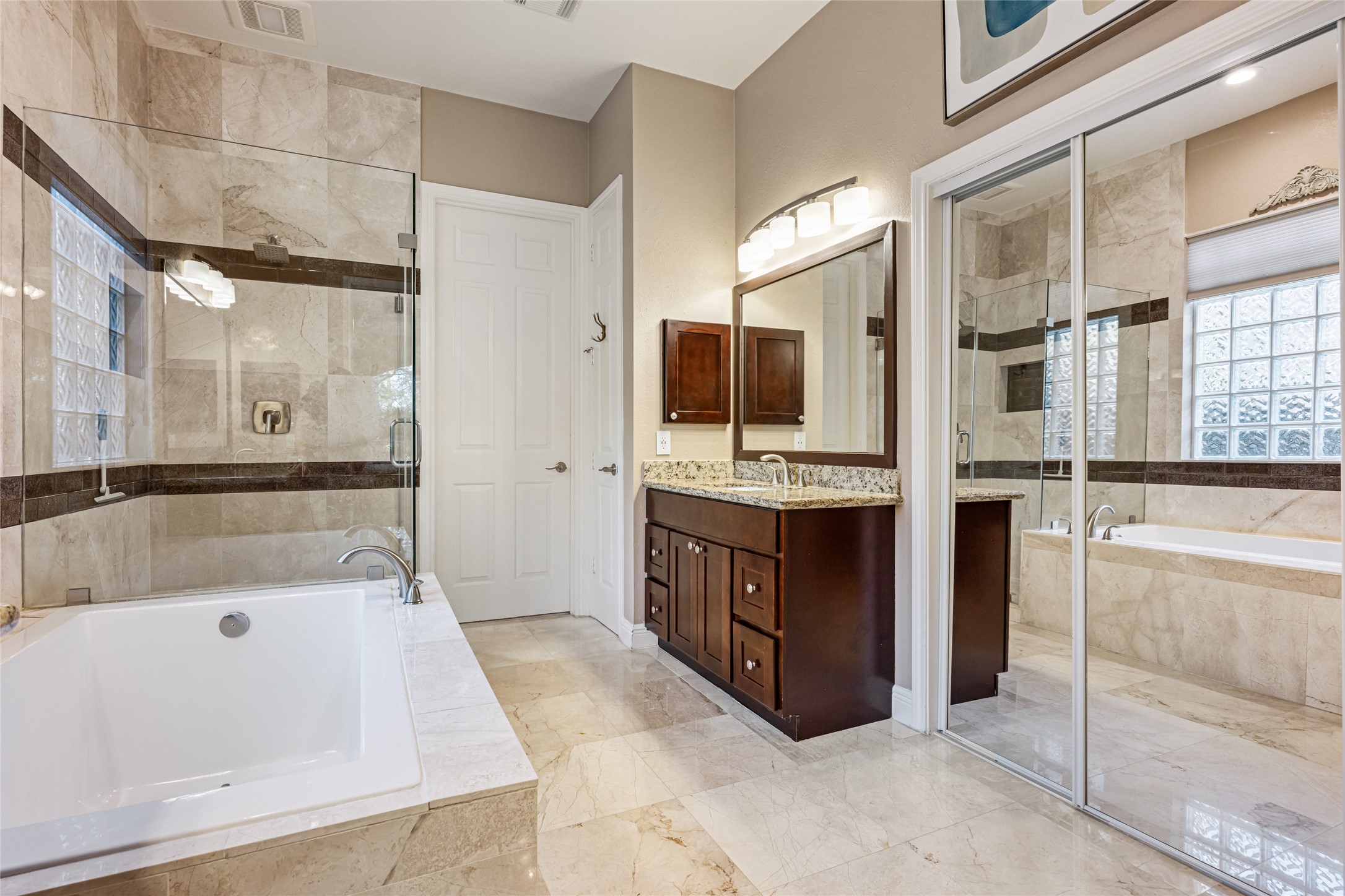 22806 2 Rivers Lane Katy, TX 77450 - Photo 30 of 49 This bathroom features a luxurious design with a spacious bathtub, glass-enclosed shower, and elegant travertine tile. The double vanity with granite countertops and ample cabinetry provides both style and functionality. Large mirrors and modern lighting enhance the room's brightness, while a sliding glass door adds a touch of sophistication.