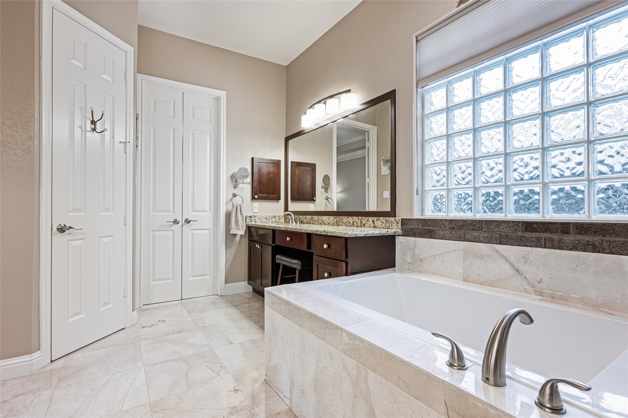 22806 2 Rivers Lane Katy, TX 77450 - Photo 32 of 49 This spacious primary bathroom features a luxurious soaking tub, elegant granite countertops, and a large vanity with ample storage. It has a modern aesthetic with neutral tones and abundant natural light from a glass block window.