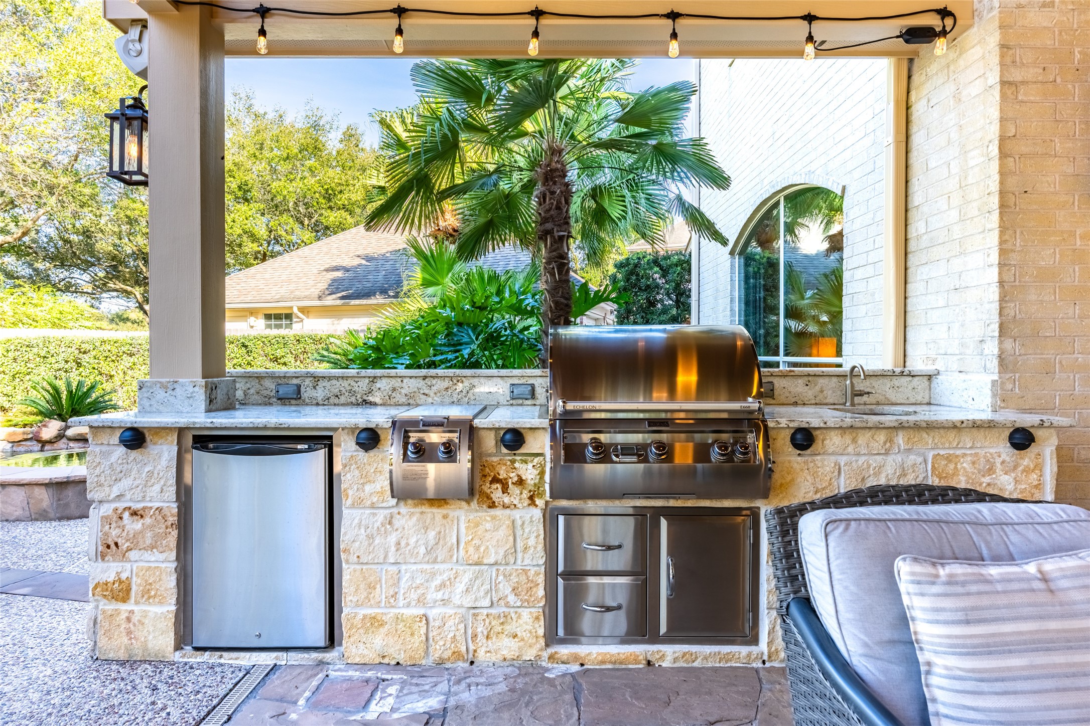 22806 2 Rivers Lane Katy, TX 77450 - Photo 40 of 49 Stylish outdoor kitchen featuring a stainless steel grill, mini-fridge, and sink set within a stone countertop. The area is well-lit with string lights and surrounded by lush greenery, offering a perfect space for entertaining.