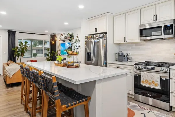 a kitchen with stainless steel appliances granite countertop a stove a refrigerator a microwave a dining table and chairs with wooden floor