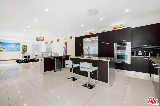a living room with stainless steel appliances furniture a flat screen tv and kitchen view