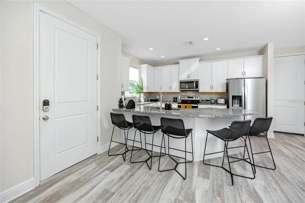 a kitchen with stainless steel appliances kitchen island granite countertop a refrigerator a stove a sink and white cabinets with wooden floor