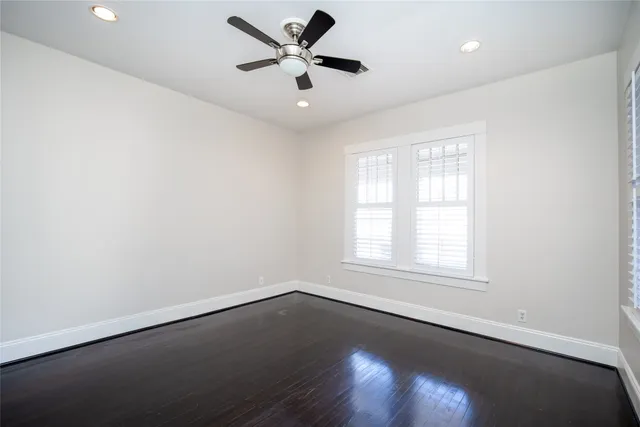 an empty room with wooden floor fan and windows