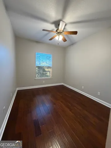 an empty room with wooden floor chandelier fan and windows