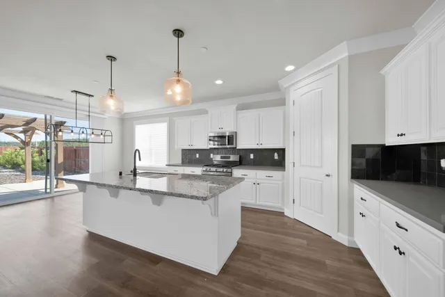 a kitchen with stainless steel appliances kitchen island granite countertop a stove a sink and white cabinets with wooden floor