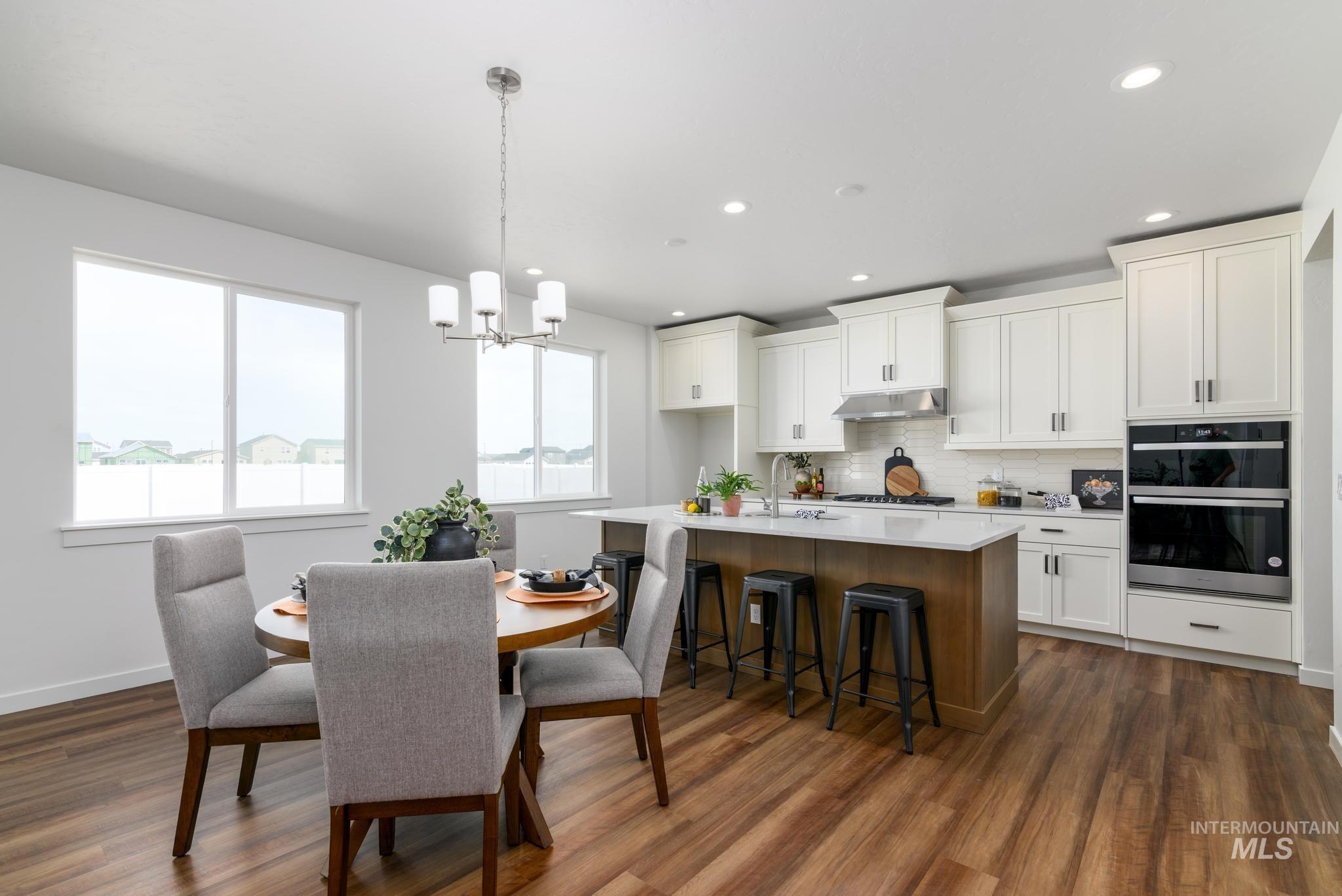 6049 West Snow Currant Street Meridian, ID 83646 - Photo 4 of 12 Two tone kitchen featuring a kitchen island with sink, hanging lights, a breakfast bar, dark wood-style floors, and two tone cabinets