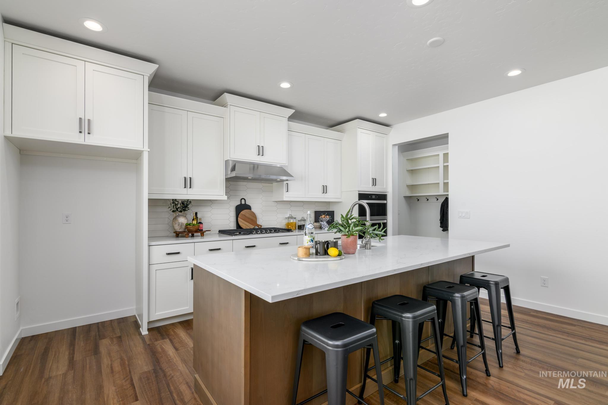 6049 West Snow Currant Street Meridian, ID 83646 - Photo 5 of 12 Two tone kitchen with two tone color scheme, a breakfast bar area, a center island with sink, dark wood-style flooring, and light stone countertops