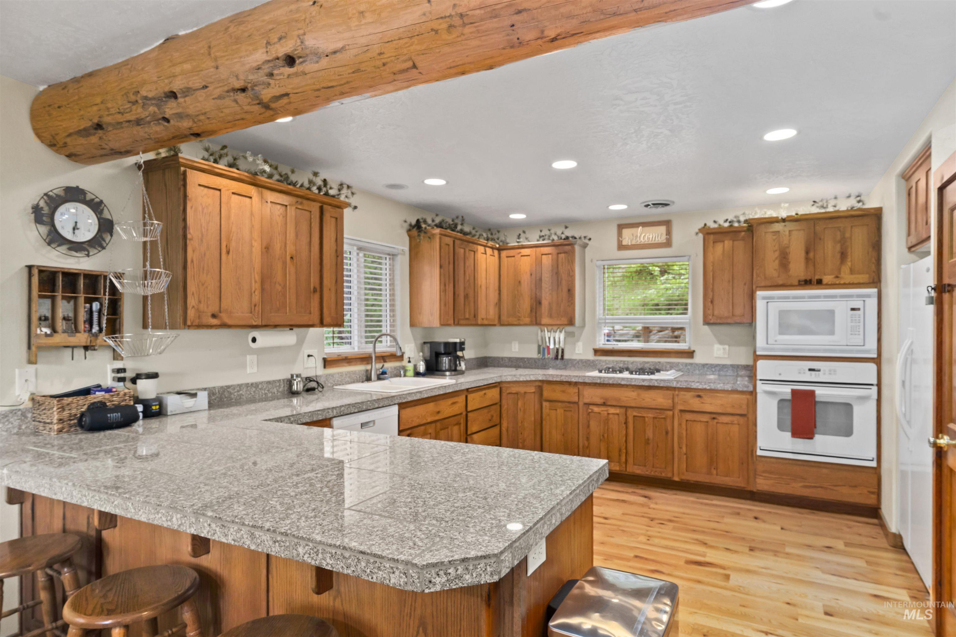 9 Deer Valley Road Garden Valley, ID 83622 - Photo 11 of 22 Kitchen featuring a U-shaped granite-finish countertop, light wood cabinetry, wood-finish flooring, recessed lighting, and a prominent exposed wood beam
