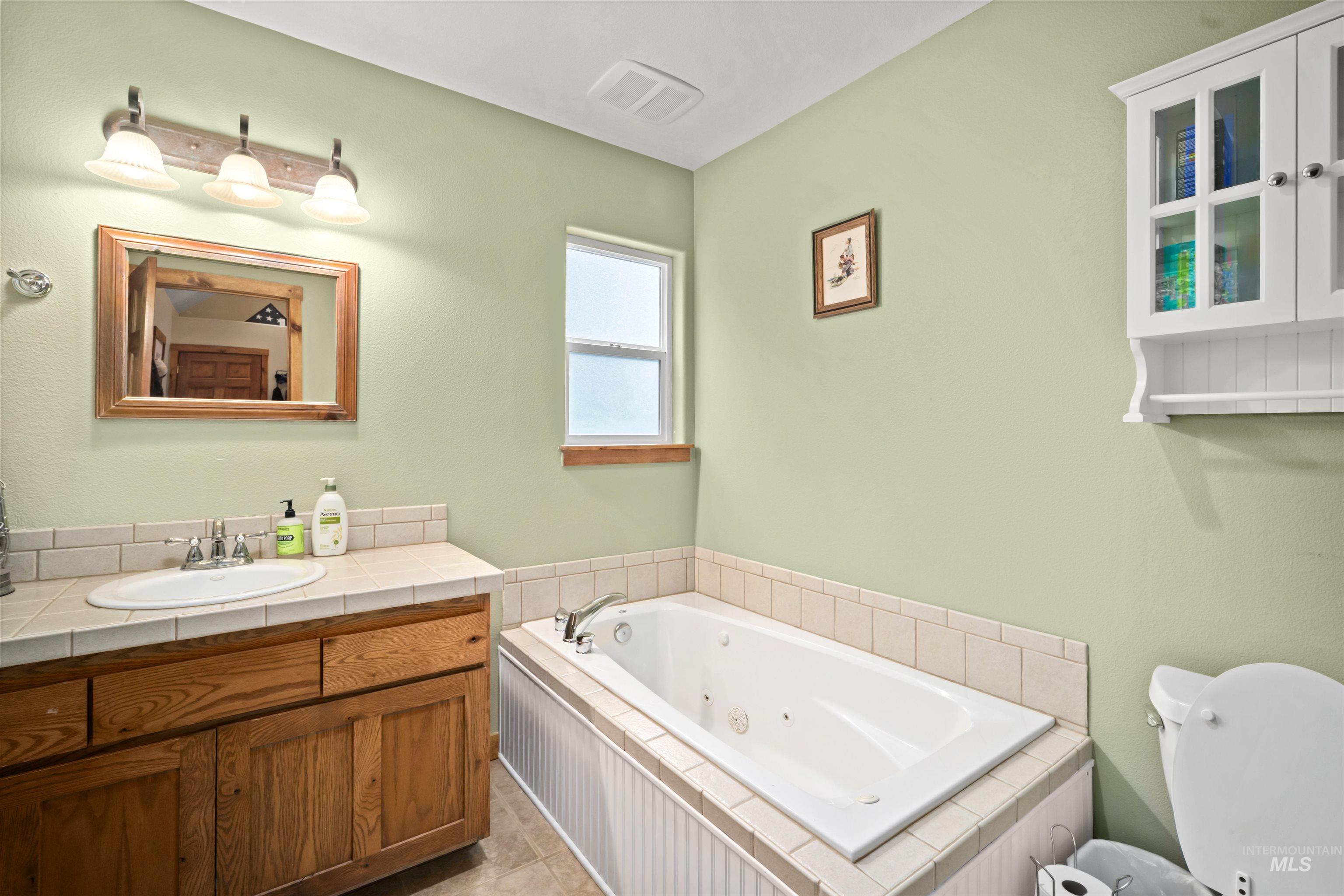 9 Deer Valley Road Garden Valley, ID 83622 - Photo 13 of 22 Bathroom featuring a built-in jetted tub with tiled surround, a wood-finish vanity with a drop-in sink and tiled countertop, a framed mirror, and a wall-mounted medicine cabinet