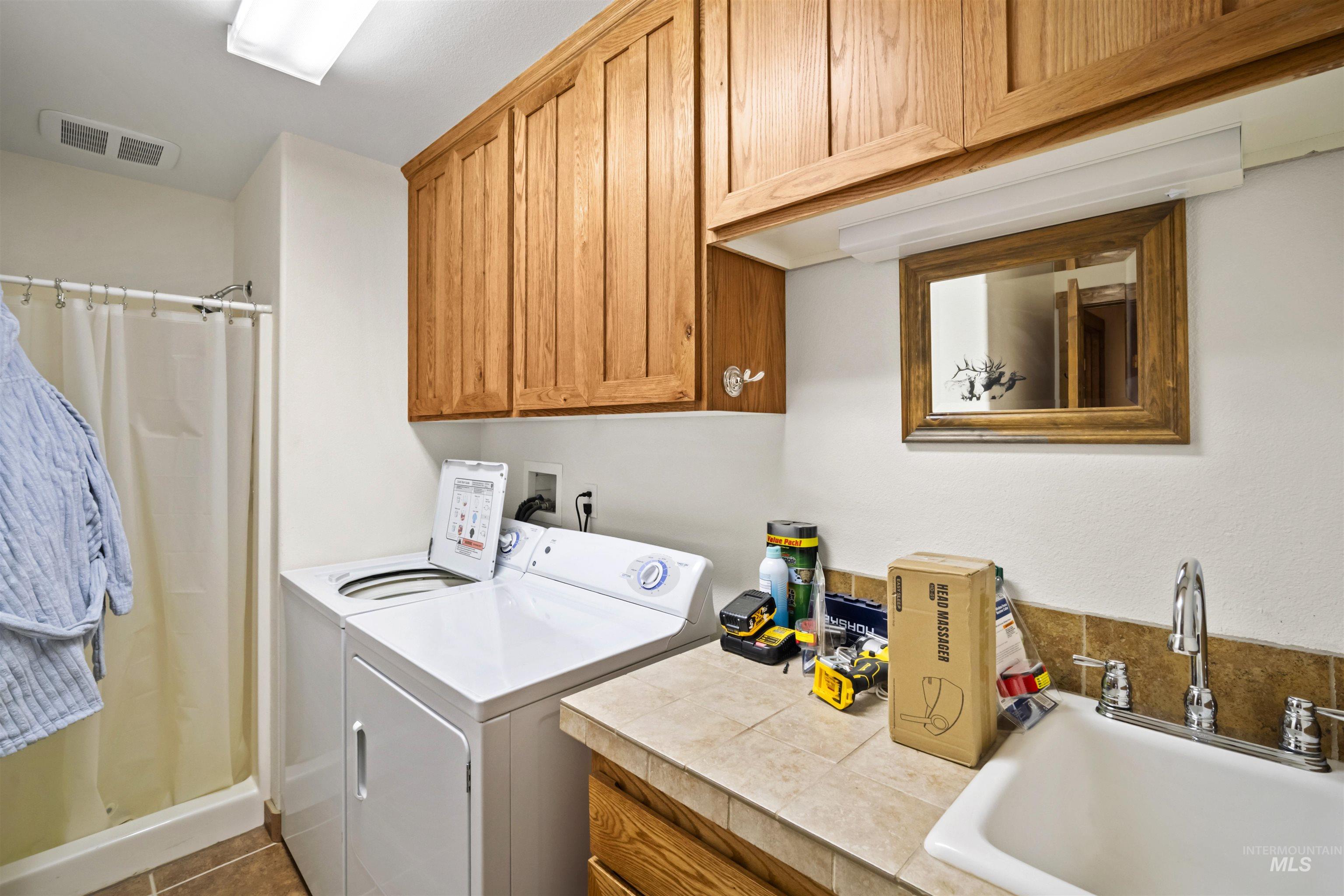 9 Deer Valley Road Garden Valley, ID 83622 - Photo 20 of 22 Functional utility room featuring a built-in shower stall, ample wood cabinetry, a utility sink with a chrome faucet, and a tiled countertop