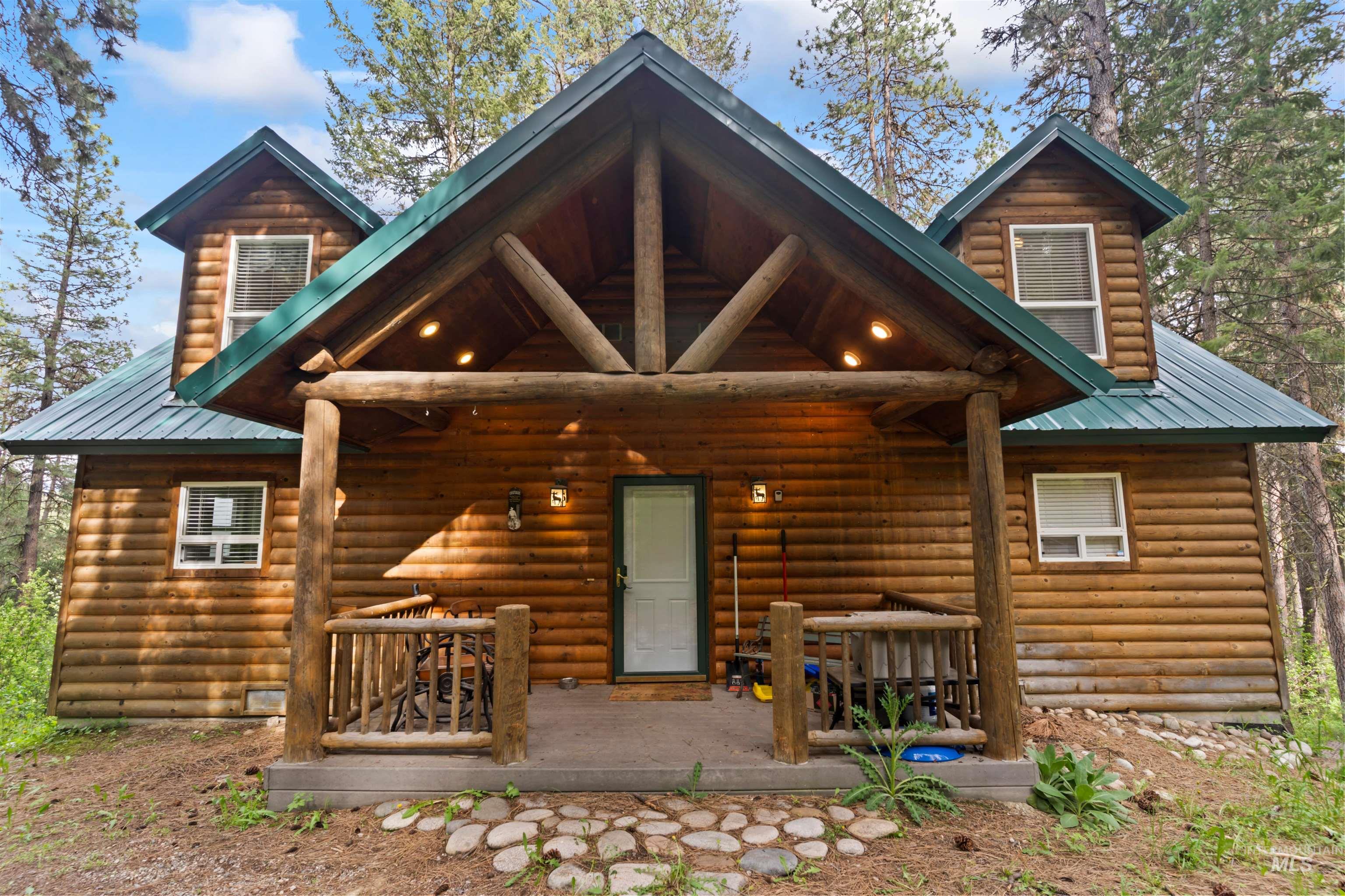 9 Deer Valley Road Garden Valley, ID 83622 - Photo 2 of 22 Log cabin exterior featuring a covered porch with exposed log beams, a prominent green metal roof, and dormer windows