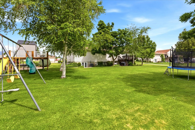 5321 South 3100th Street West Roy, UT 84067 - Photo 59 of 64 Spacious green lawn with mature trees, a multi-level deck, and a play structure featuring a slide