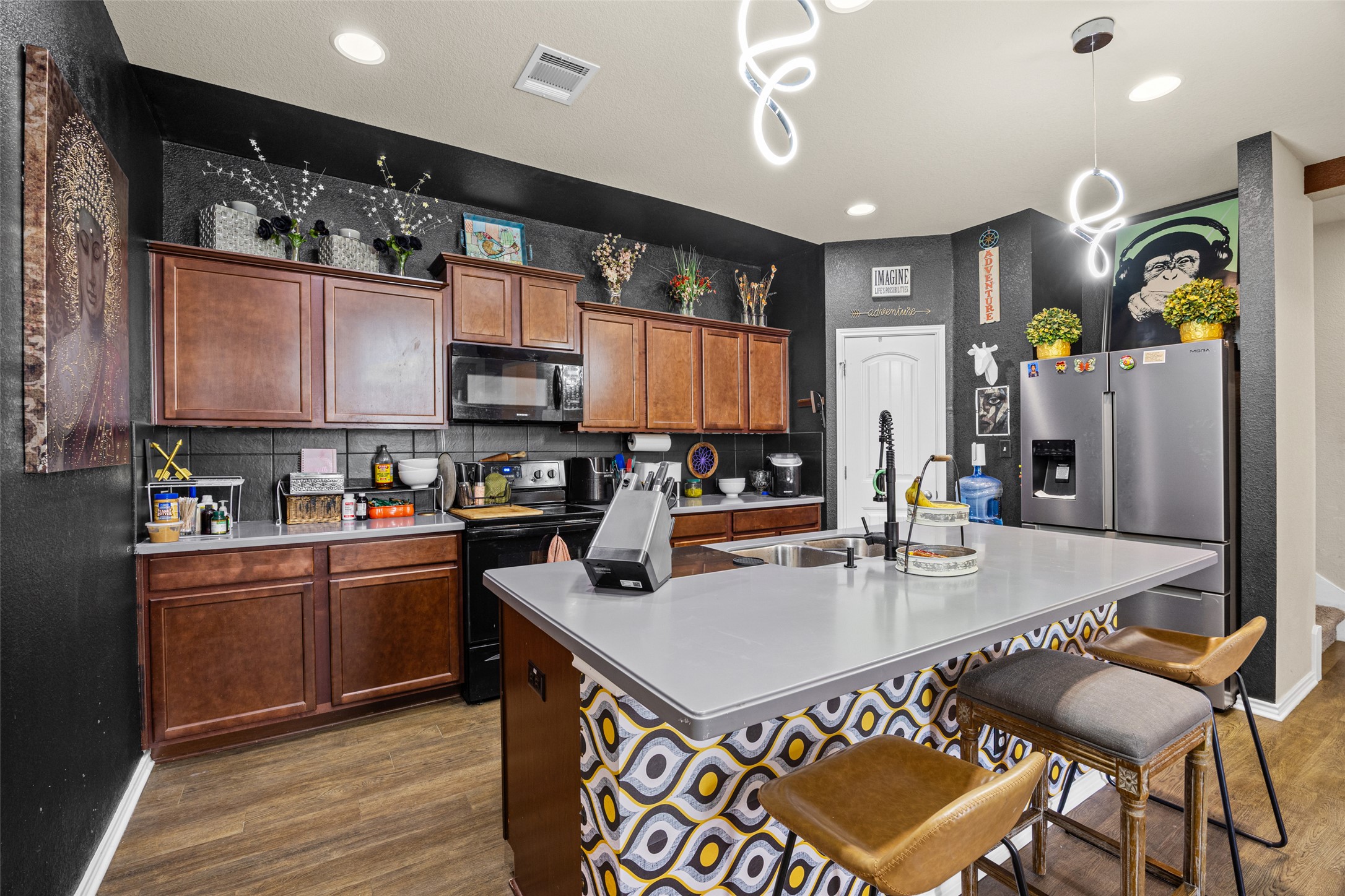 19113 Rookery Trail Pflugerville, TX 78660 - Photo 24 of 36 Contemporary kitchen featuring a central island with an undermount sink, dark wood cabinetry, black appliances, wood-finish flooring, and recessed ceiling lighting