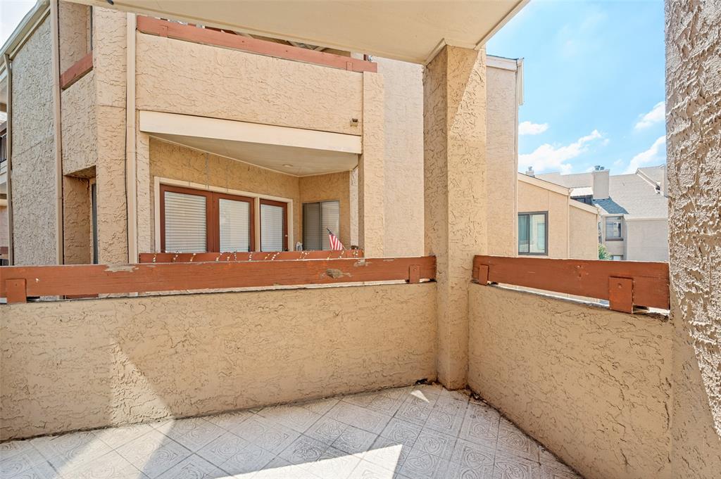 5550 Spring Valley Road, Unit C21 Dallas, TX 75254 - Photo 20 of 26 Exterior balcony featuring textured stucco walls, a wood-finished railing, and patterned tile flooring