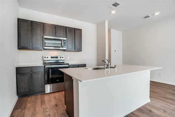a view of kitchen with microwave oven a stove and white cabinets with wooden floor