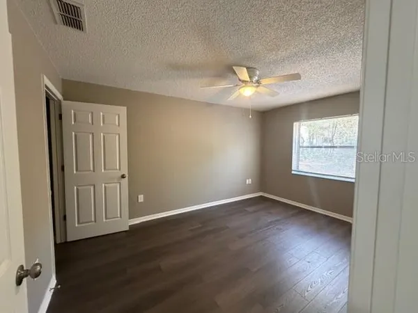 an empty room with wooden floor chandelier fan and windows
