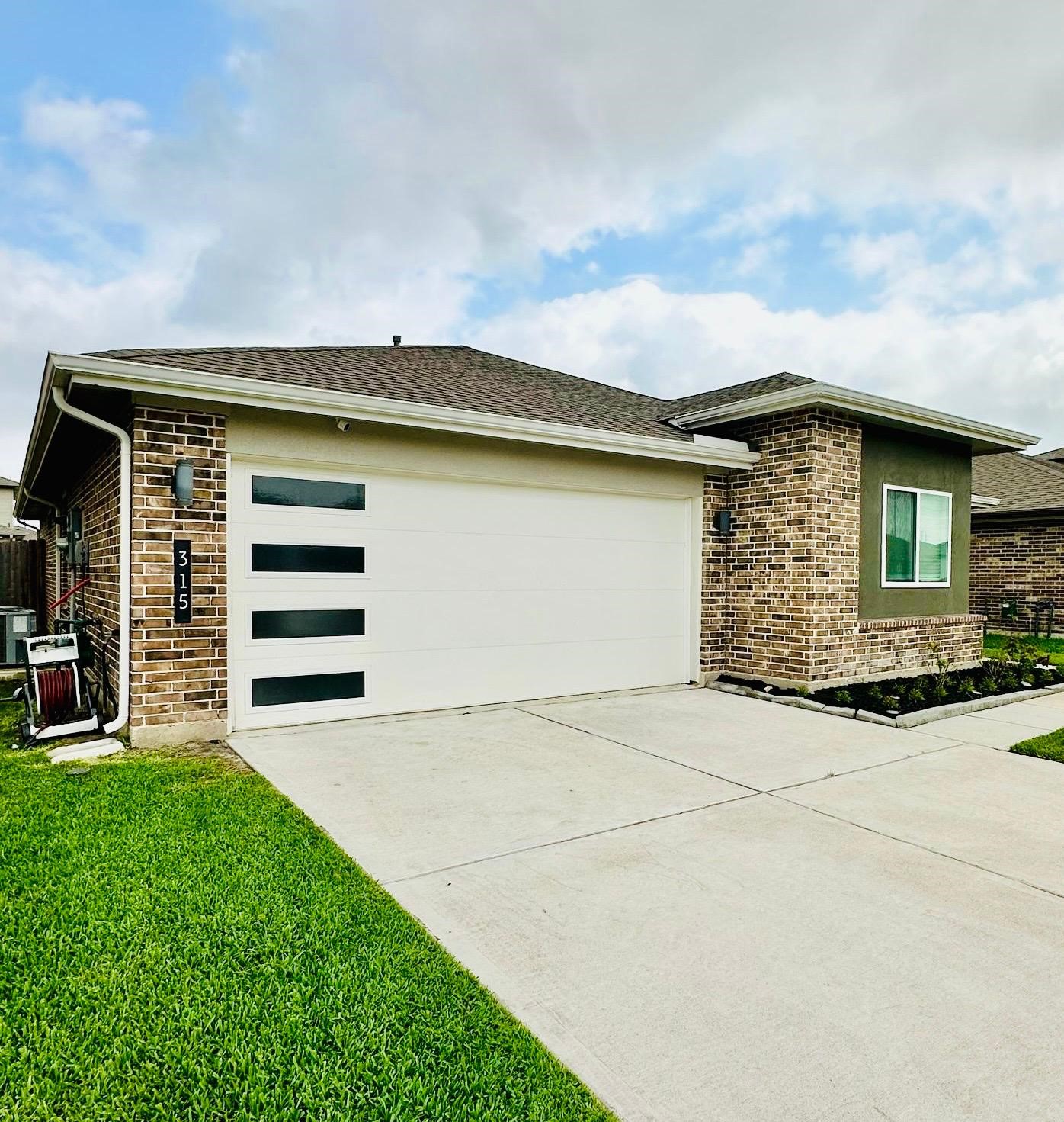 This is a modern single-story home with a brick exterior, a two-car garage featuring sleek horizontal windows, and a well-maintained front yard.