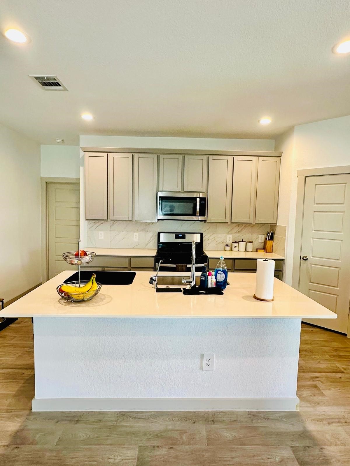 315 John House Lane Rosharon, TX 77583 - Photo 13 of 27 Modern kitchen with sleek light wood cabinets, a spacious island with a sink, and stainless steel appliances. The room features ample counter space, recessed lighting, and a stylish backsplash, creating a bright and inviting space for cooking and entertaining.